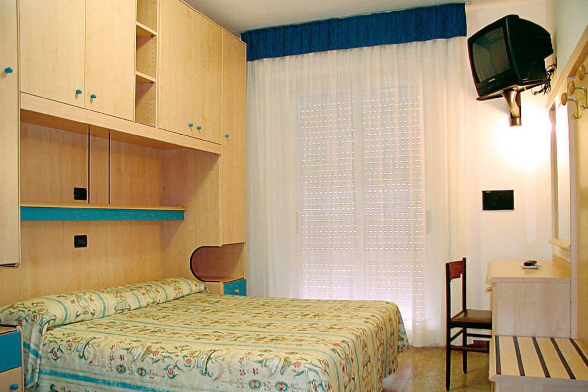 A bedroom with a bed, a desk, a chair, and a television.