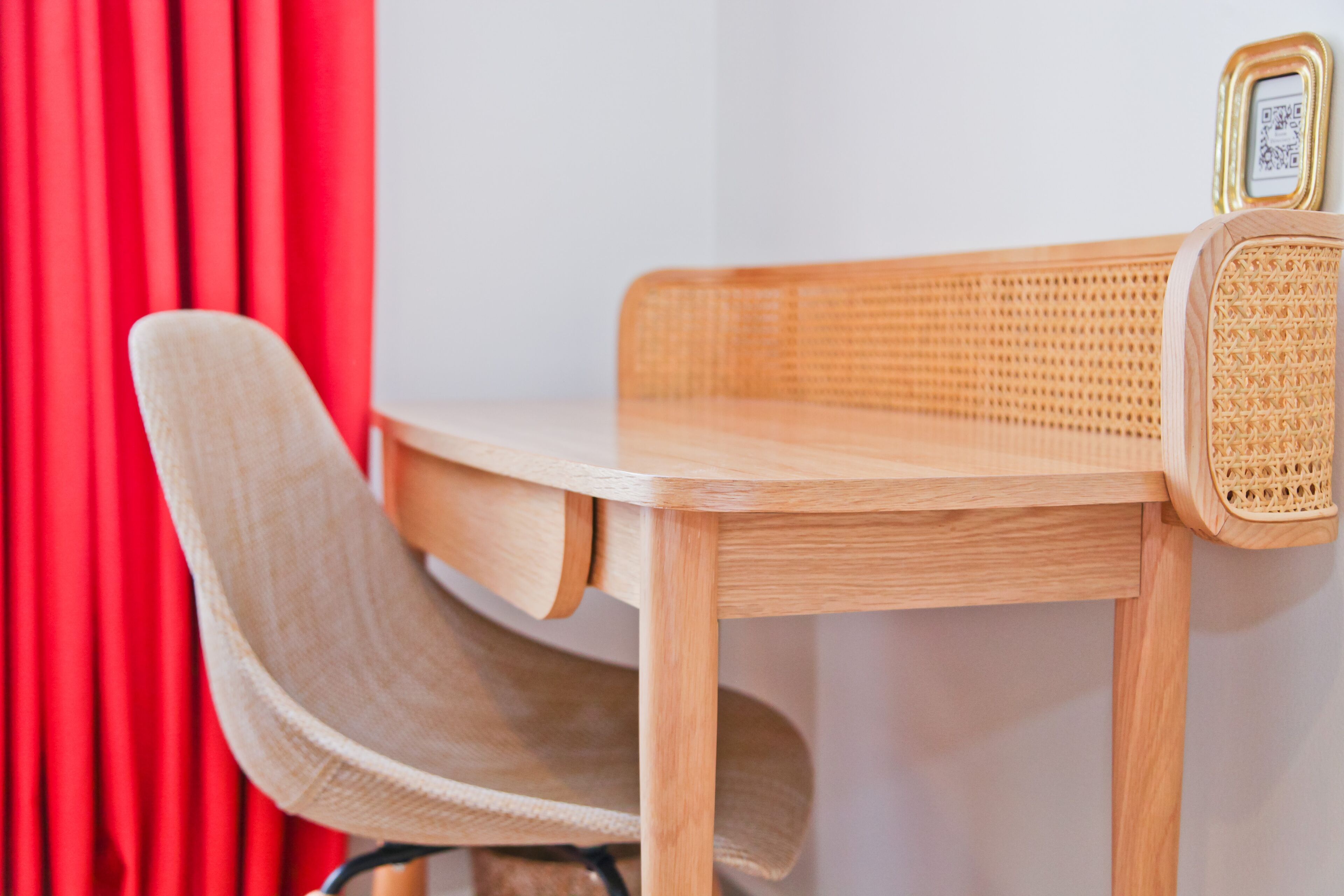A wooden desk with a woven chair and a small table lamp.