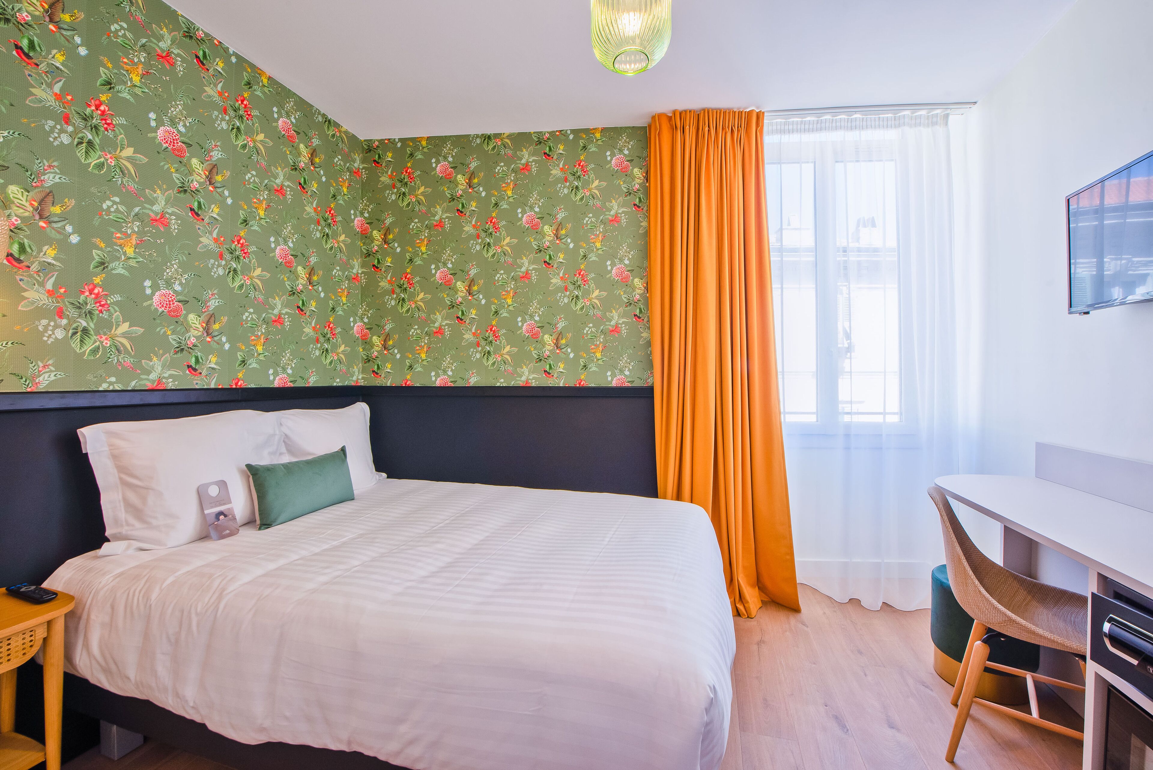 Una cama bien hecha con ropa blanca, una almohada verde y una mesita de noche con un teléfono y un control remoto.