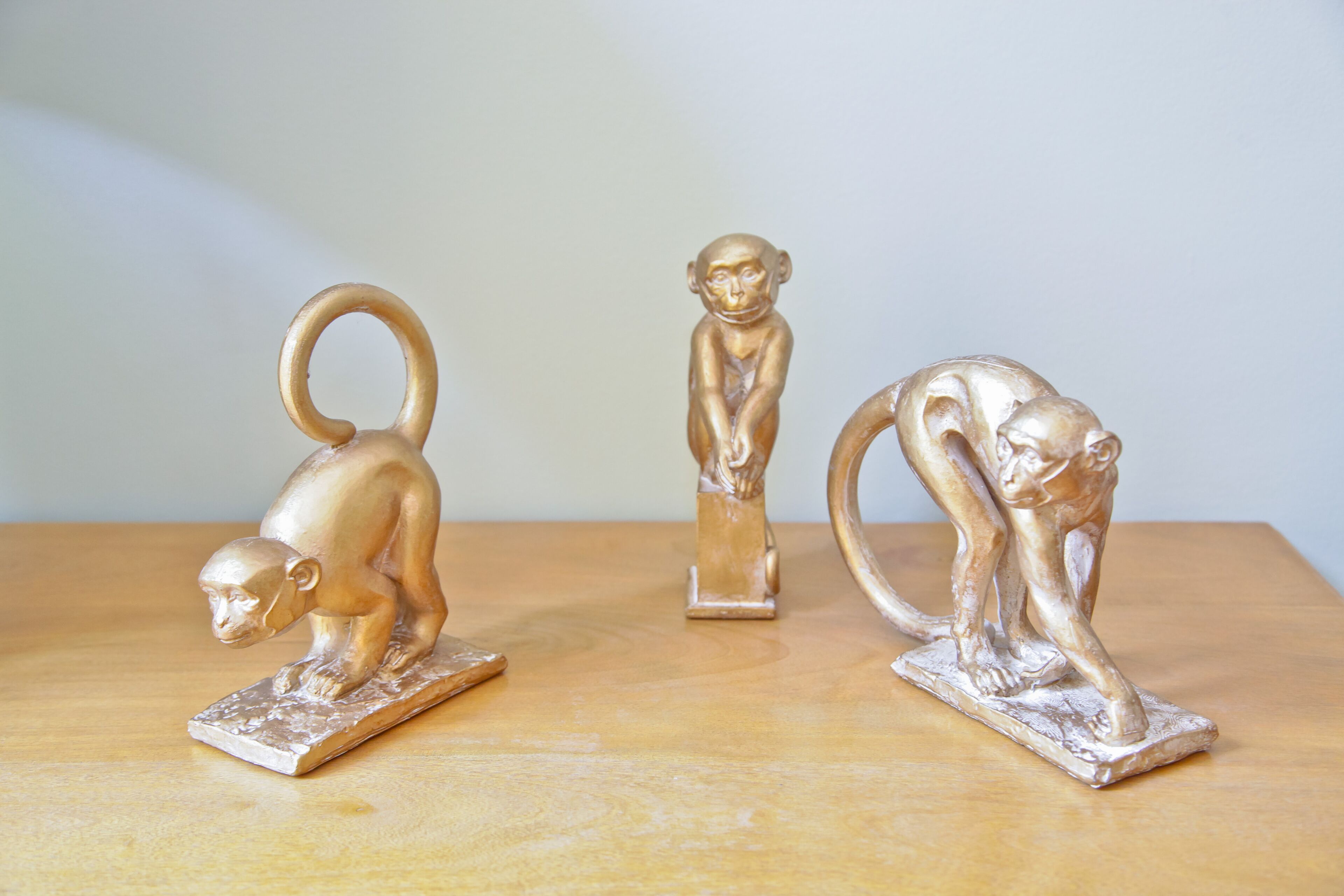 Tres esculturas metálicas de monos sobre una superficie de madera.
