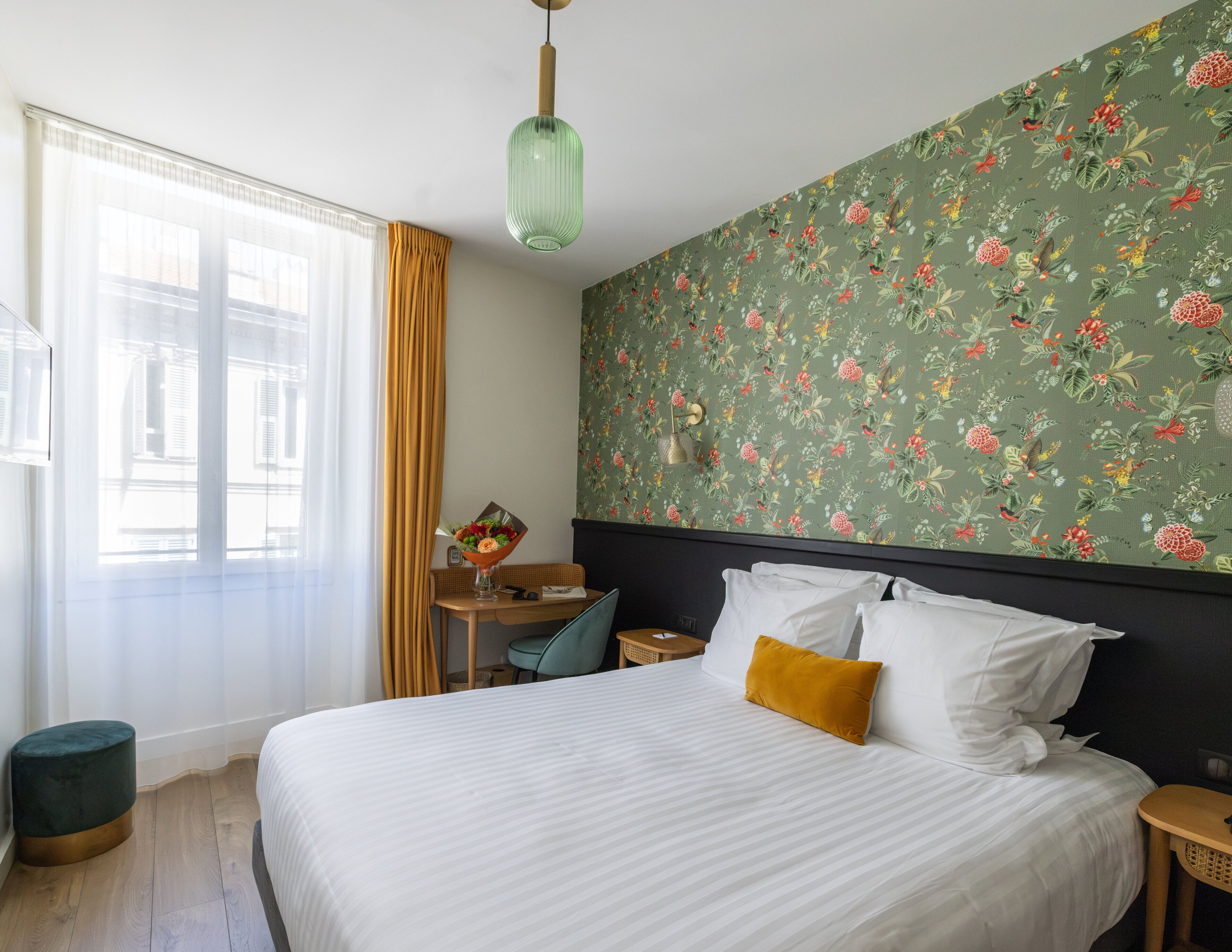 A hotel room with a bed, a desk, a chair, a small table, and a window with curtains.