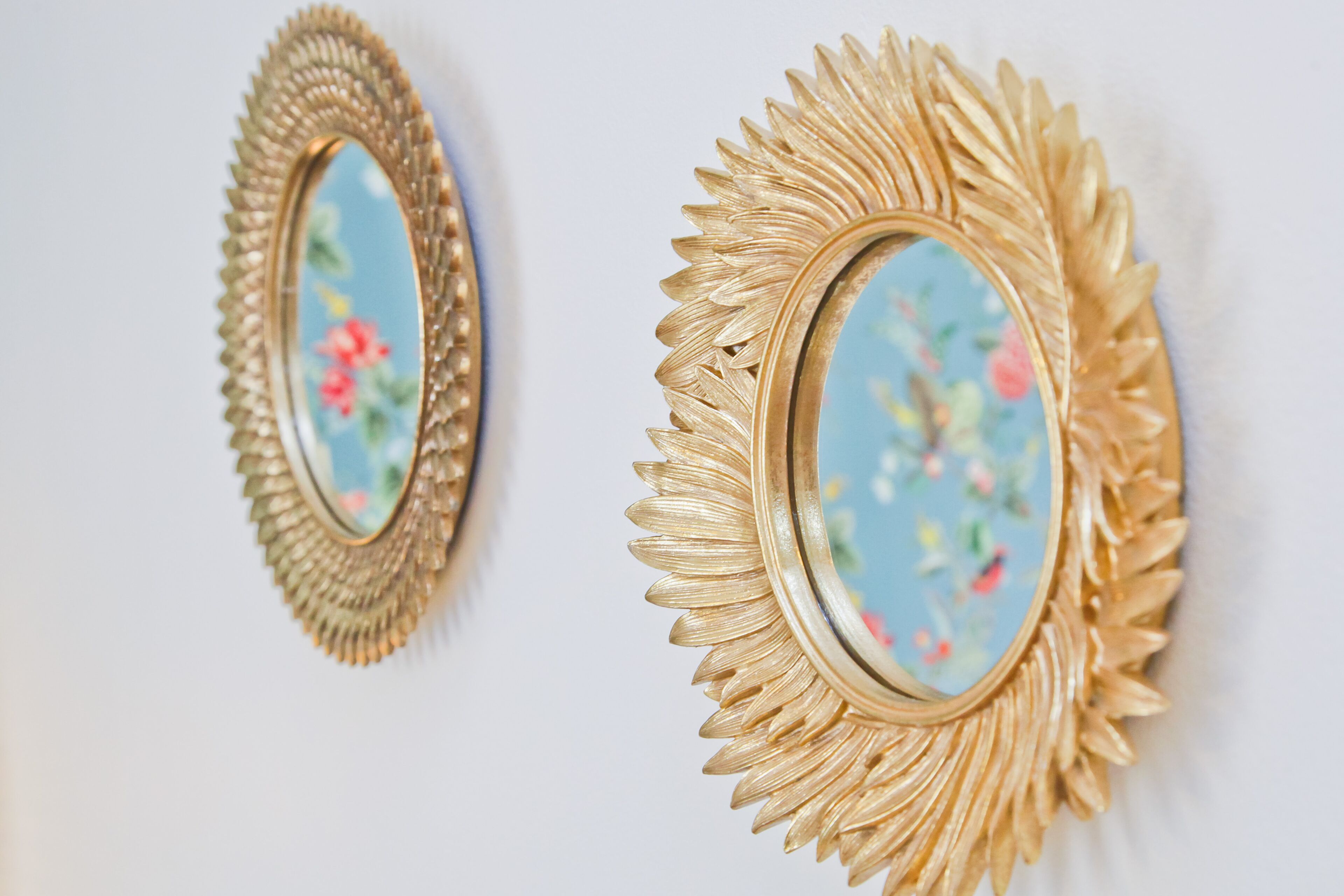 Two wall-mounted mirrors with ornate gold frames and floral designs.