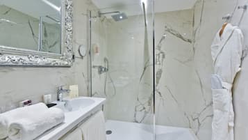 Ein modernes Badezimmer mit einer gläsernen Duschkabine, einer Marmorfliesenwand, einem weißen Waschbecken und einem großen Spiegel.