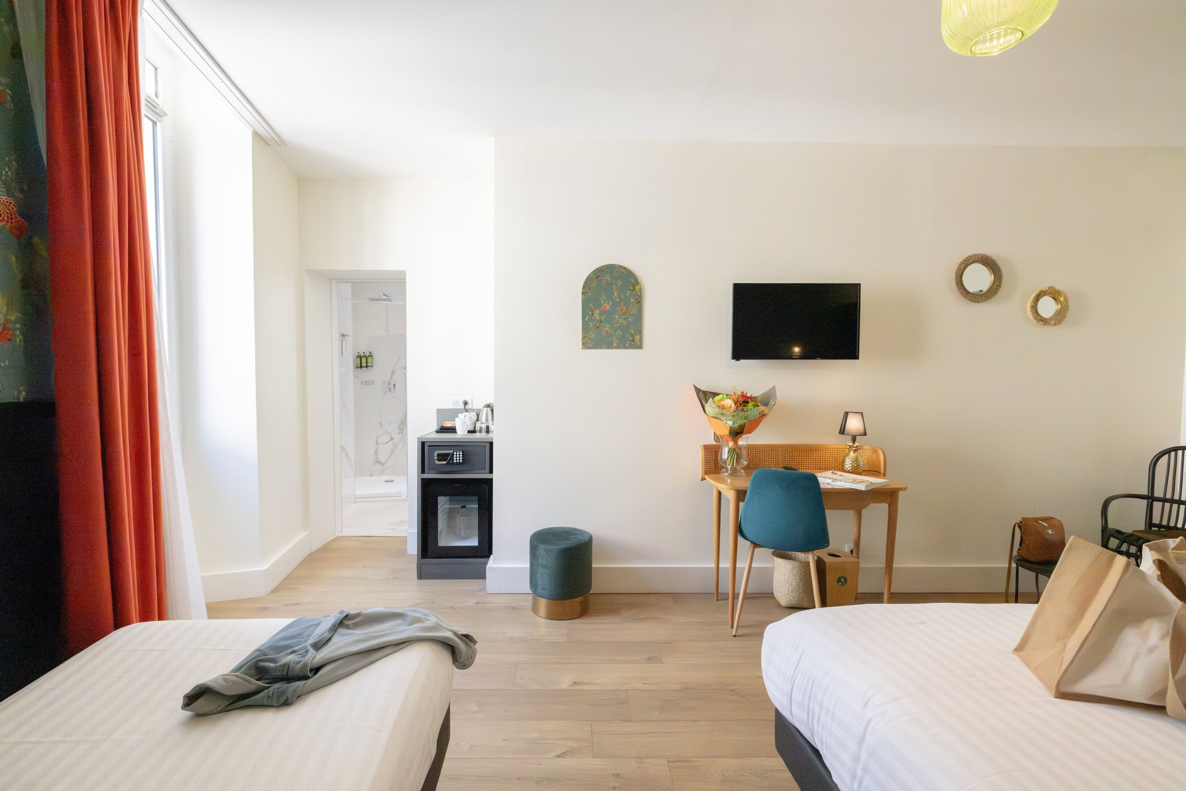 Une chambre d’hôtel avec deux lits, un bureau avec une chaise, une télévision et une petite table avec une lampe.
