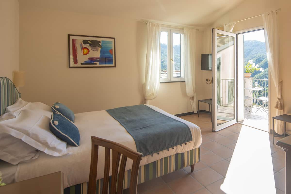 A bedroom with a bed, a chair, a TV, and a balcony with a table and chairs.