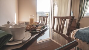 Ein Frühstückswagen mit Gebäck, einem Glas Saft und Teetassen auf einem Tisch am Fenster mit Blick auf Hügel.