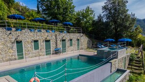 Una piscina con un muro de piedra, puertas verdes y sombrillas azules.