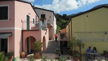 A courtyard with potted plants, a staircase leading to a balcony, and a table with two people sitting.