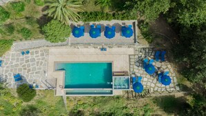 Eine Vogelperspektive zeigt ein Resort mit Schwimmbecken, Liegestühlen und Sonnenschirmen.