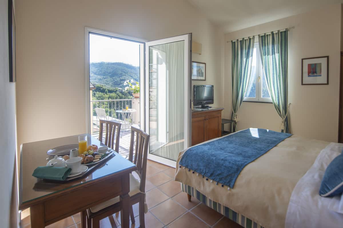 A hotel room with a balcony, a bed, a desk with breakfast, and a TV.