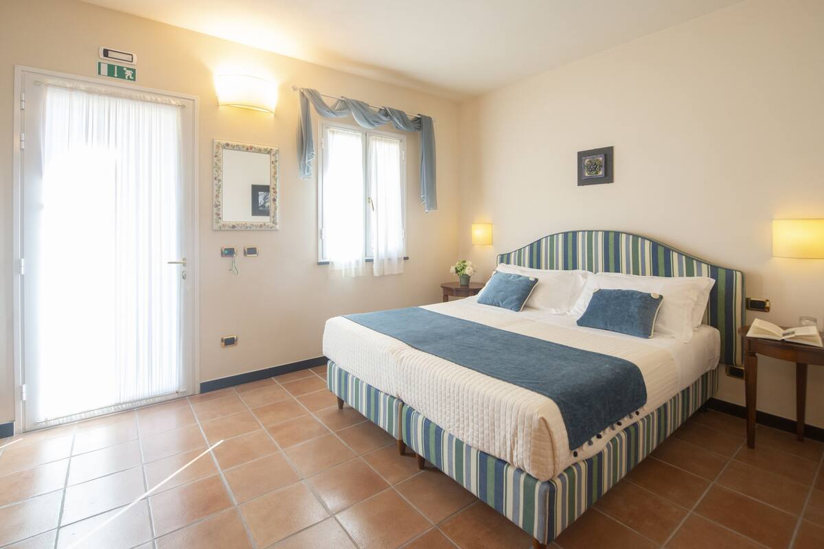 A bedroom with a bed, a bedside table, a nightstand, a mirror, and a door.