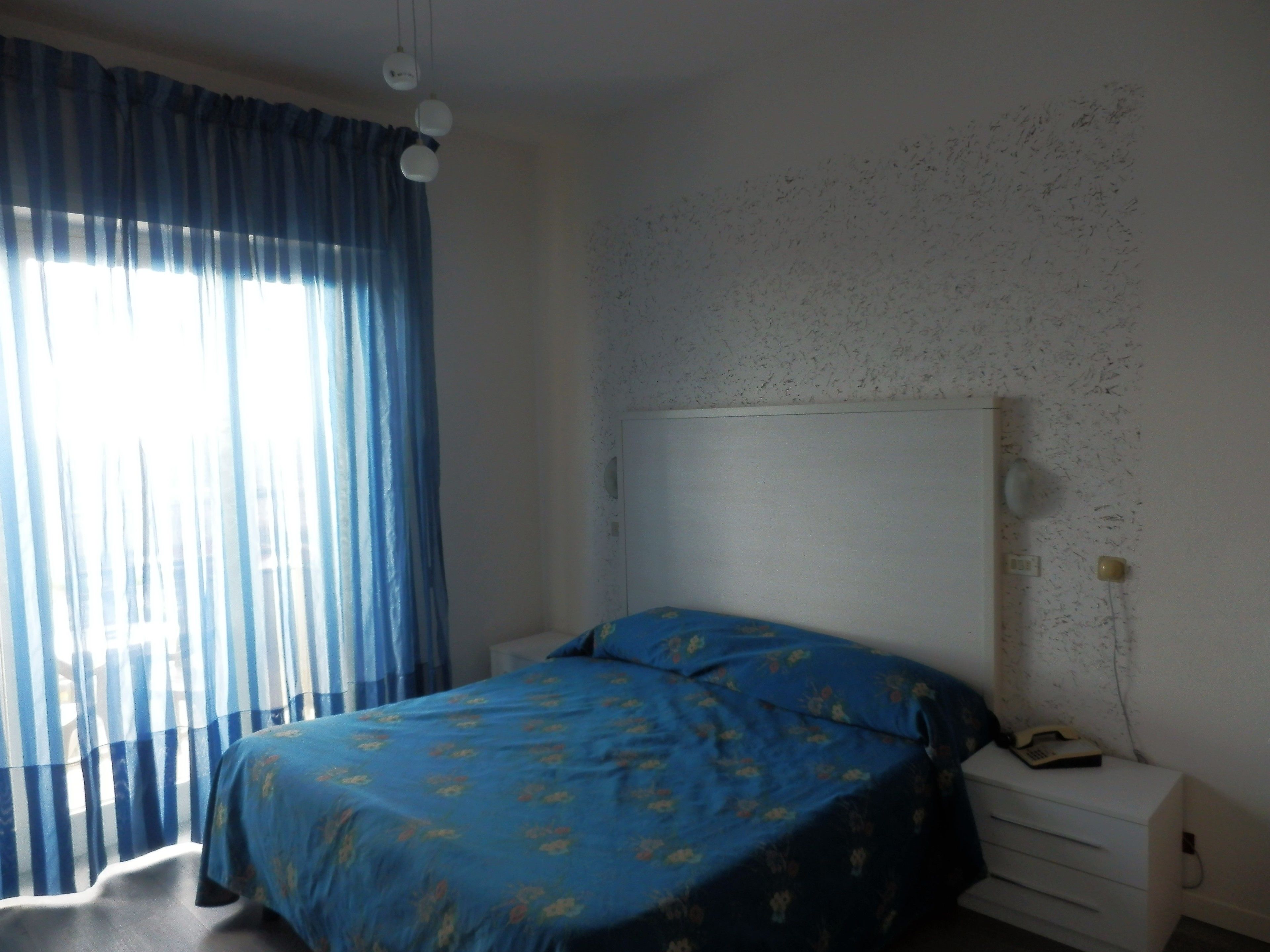 Une chambre à coucher comprenant un lit, une table de chevet, un téléphone et un mur orné d’un motif texturé.