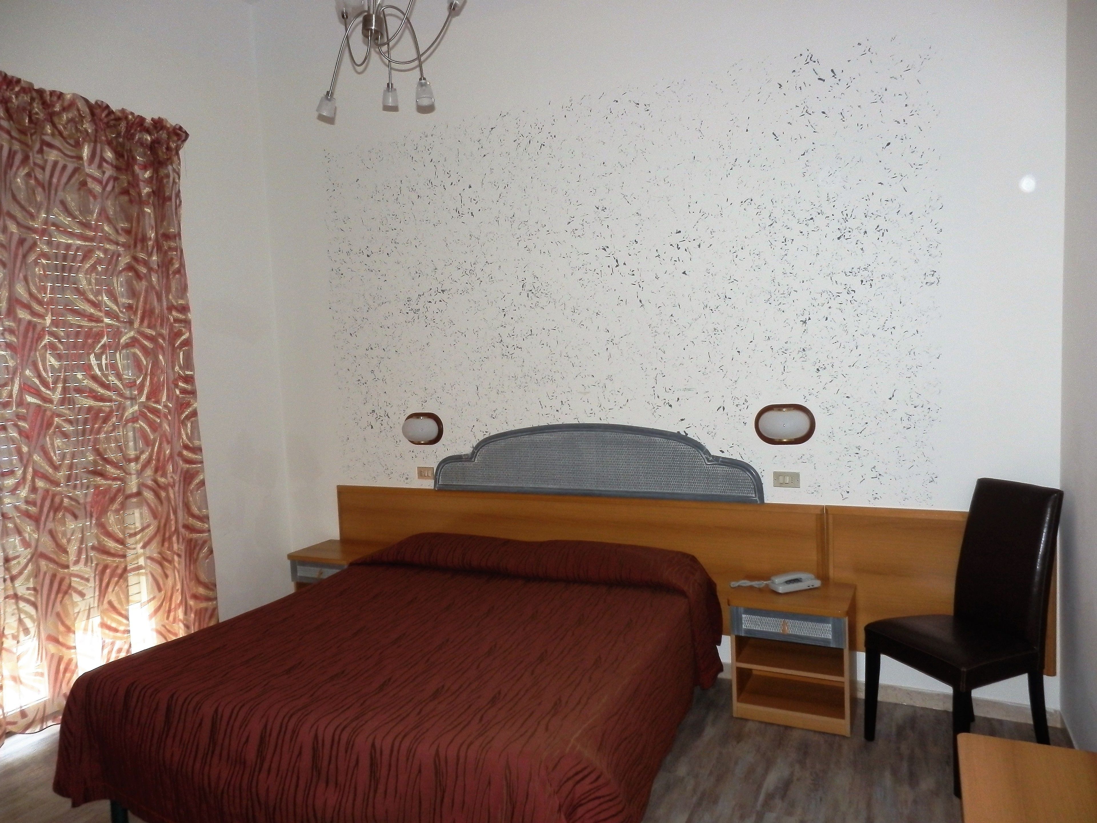 A bedroom with a wooden bed, a nightstand, a chair, and a wall-mounted lamp.