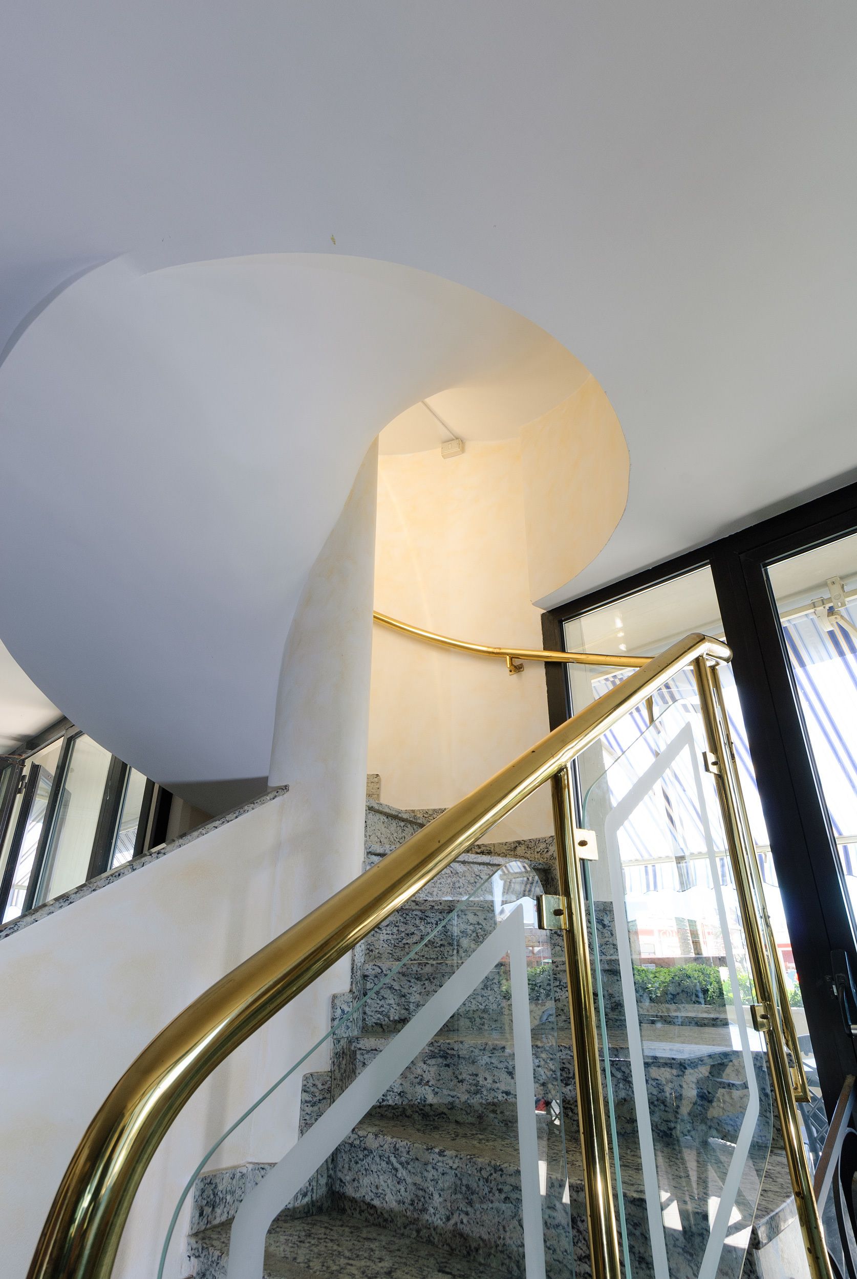 A curved staircase with a glass railing and a white wall.