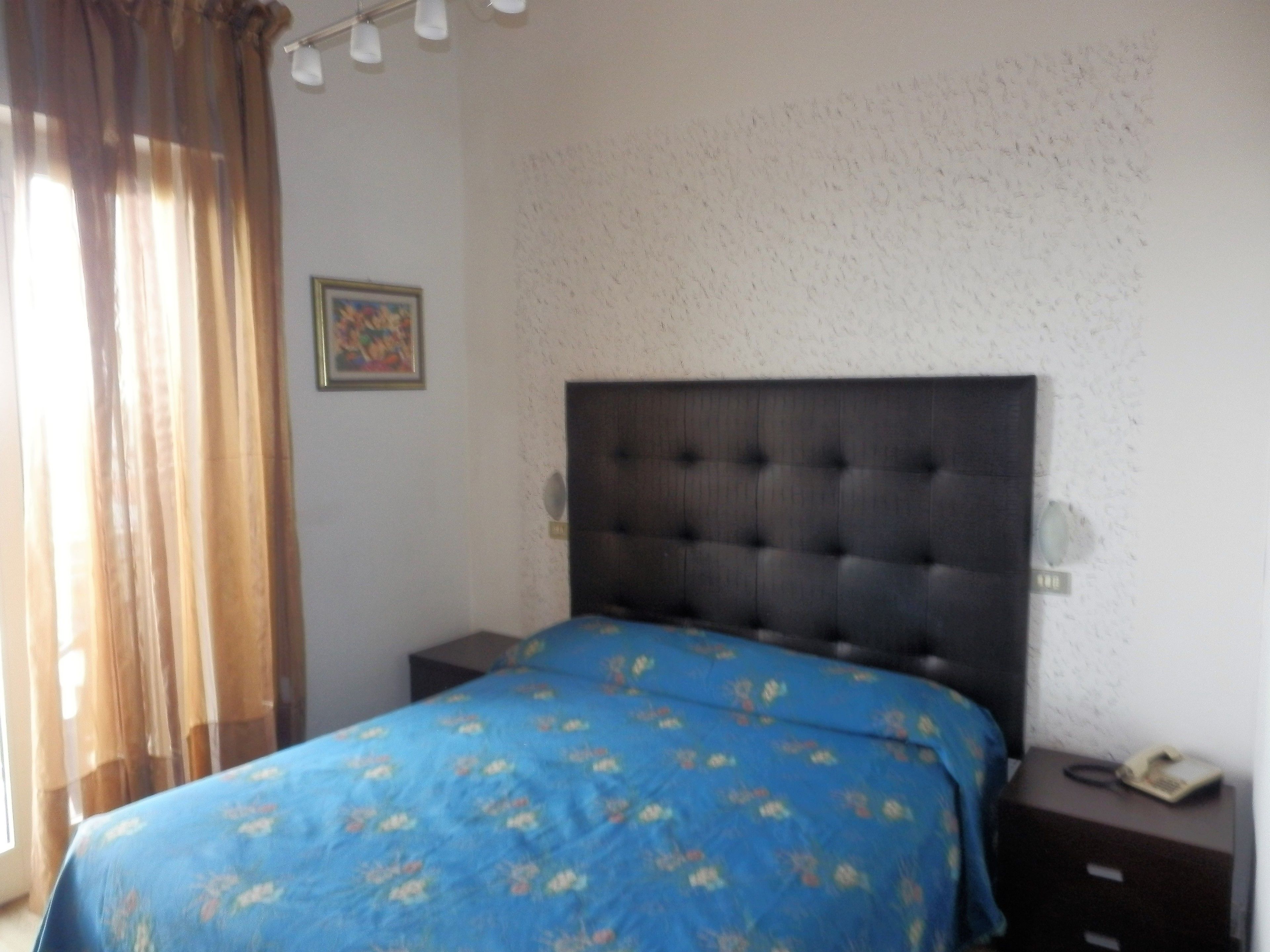 A bedroom with a bed, a nightstand, a telephone, and a window with curtains.