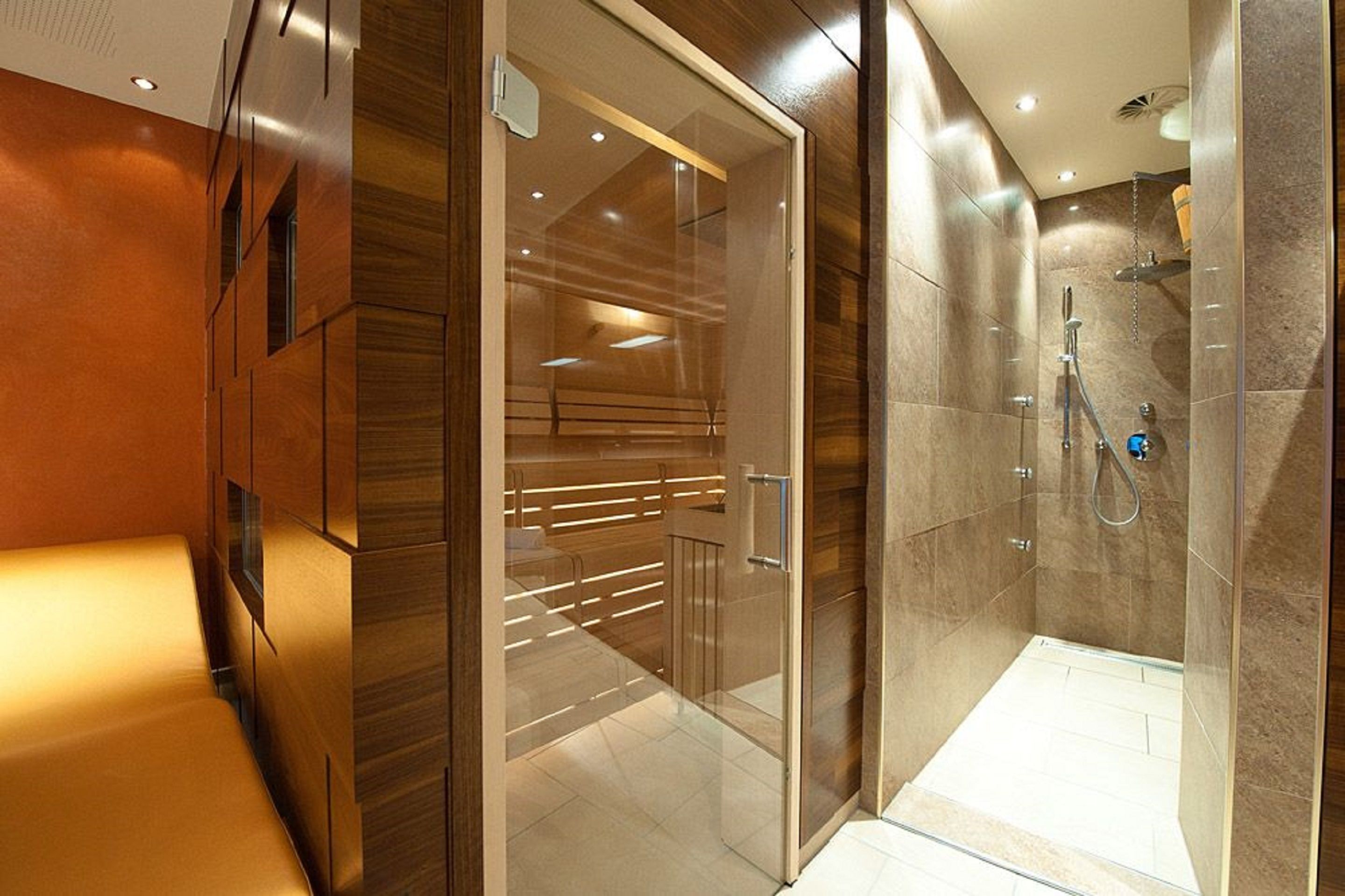 A modern bathroom with a glass shower enclosure, a wooden bench, and a glass door leading to a shower area.