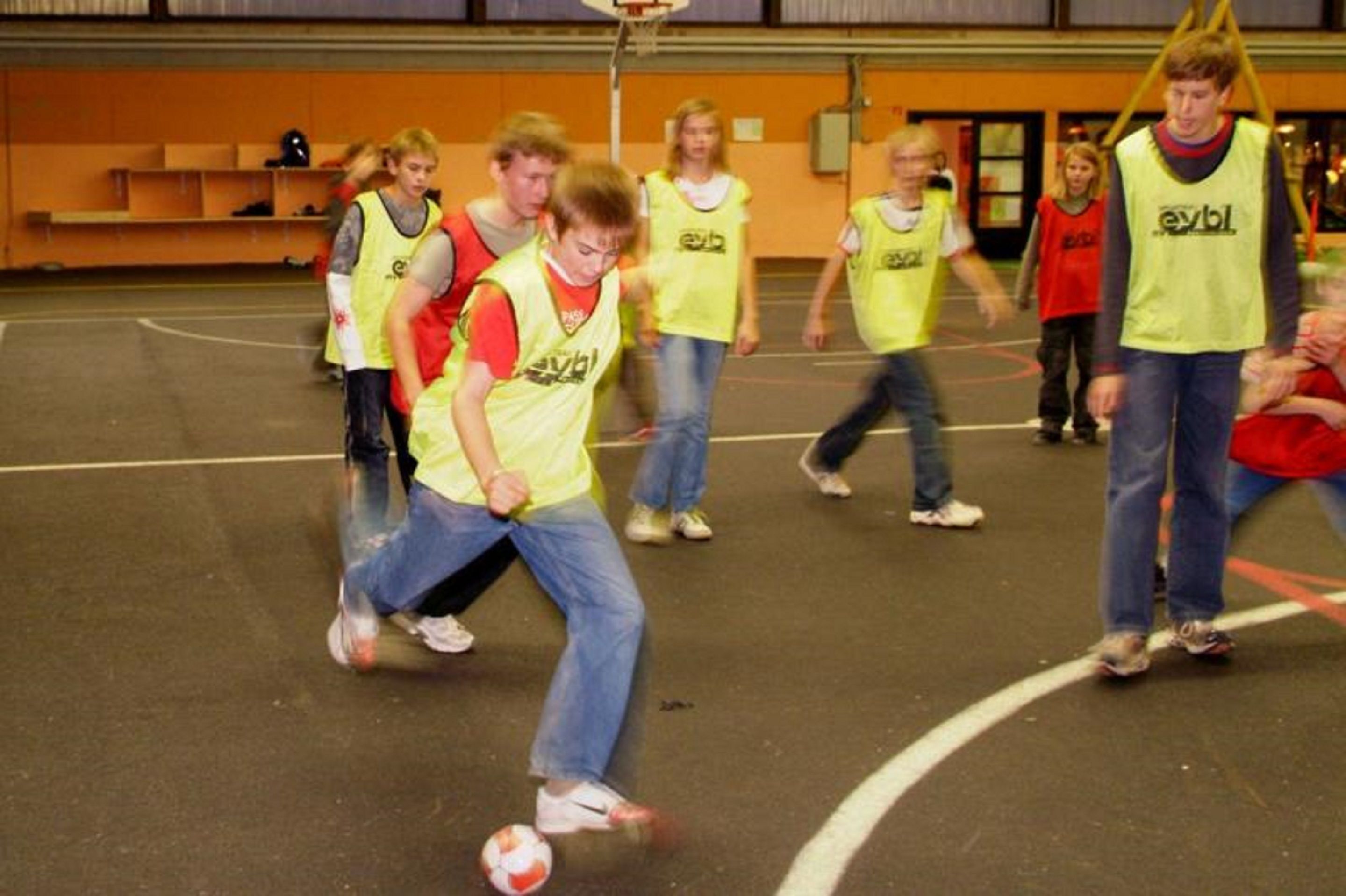 Eine Gruppe von Menschen spielt Fußball in einer Sporthalle.