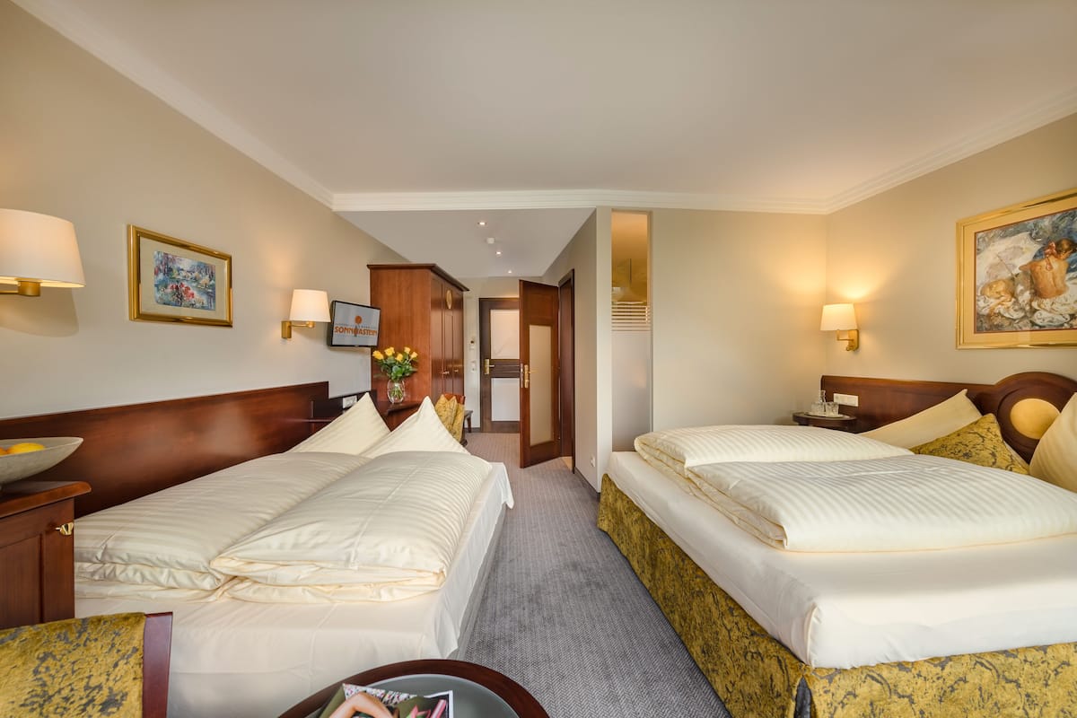 Een hotelkamer met twee bedden, een houten hoofdbord, een nachtkastje, een lamp en een ingelijst schilderij aan de muur.