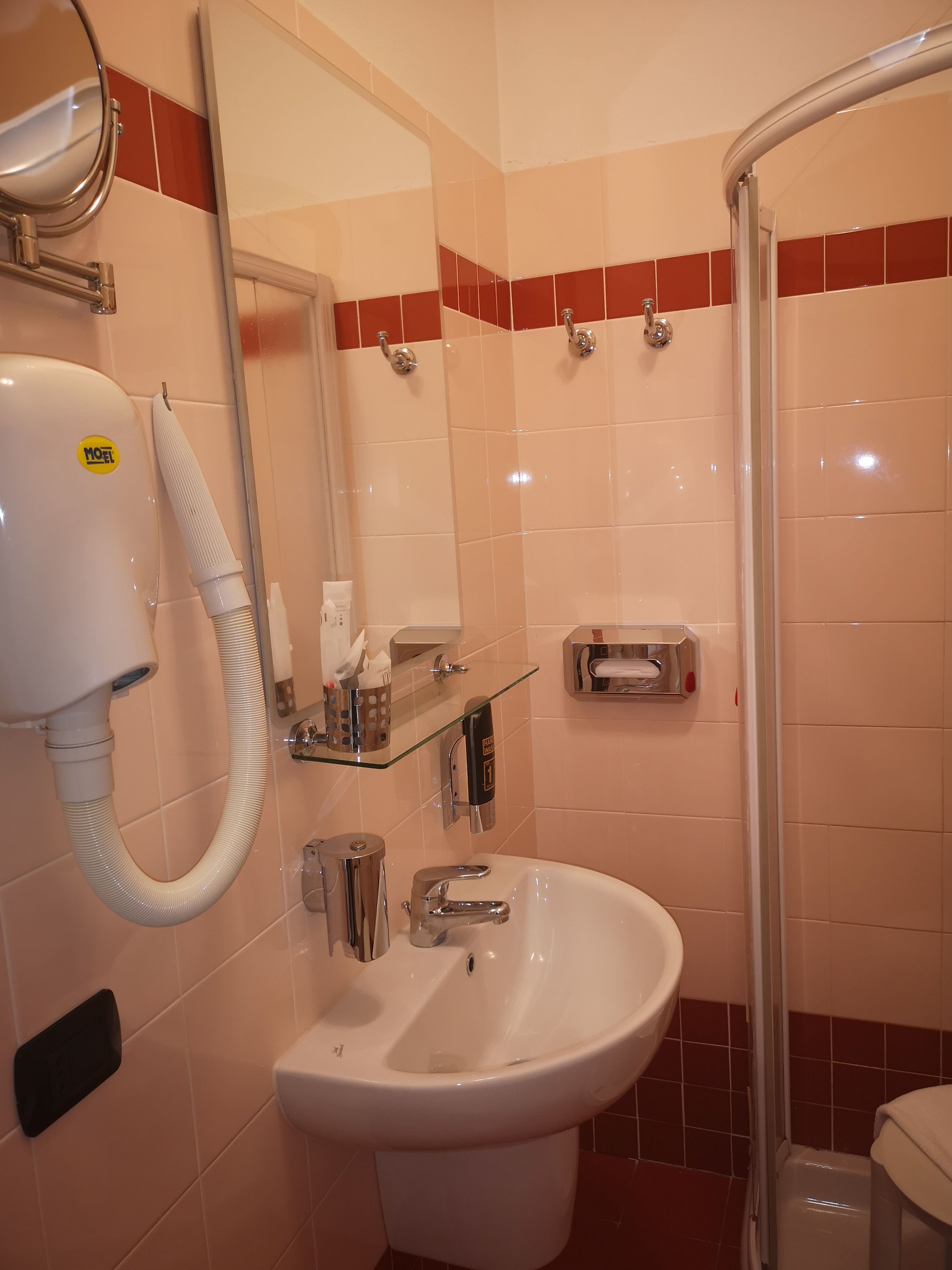 A bathroom with a white sink, a mirror, a handheld hair dryer, and a glass shower enclosure.
