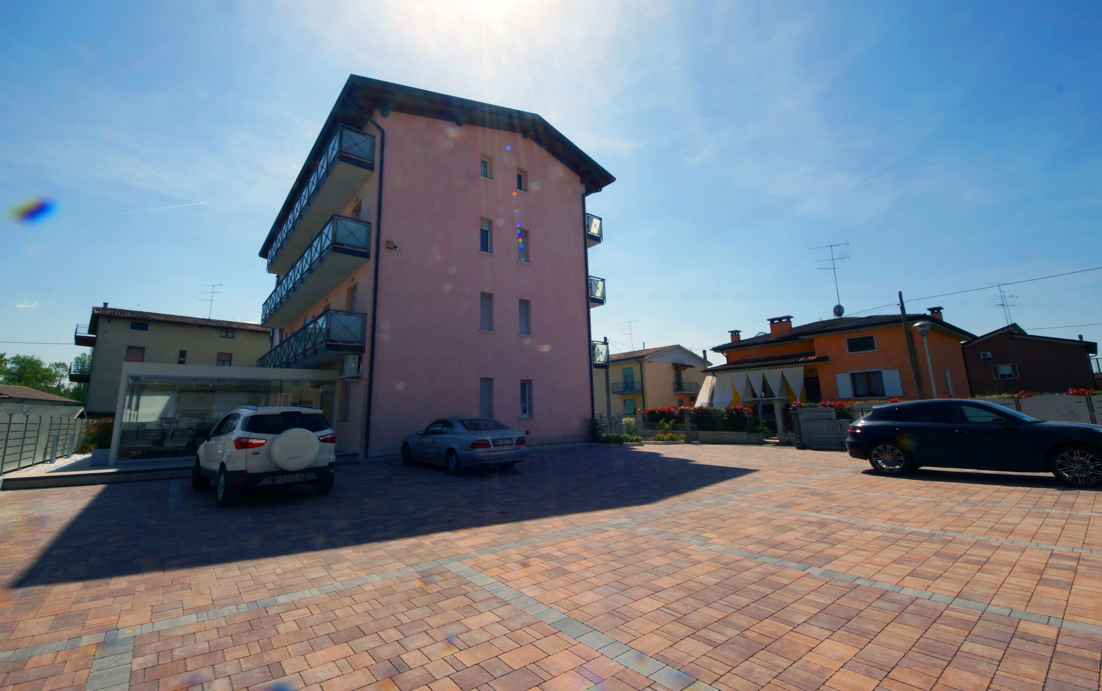 A parking area with several cars, a pink building with balconies, and adjacent houses.