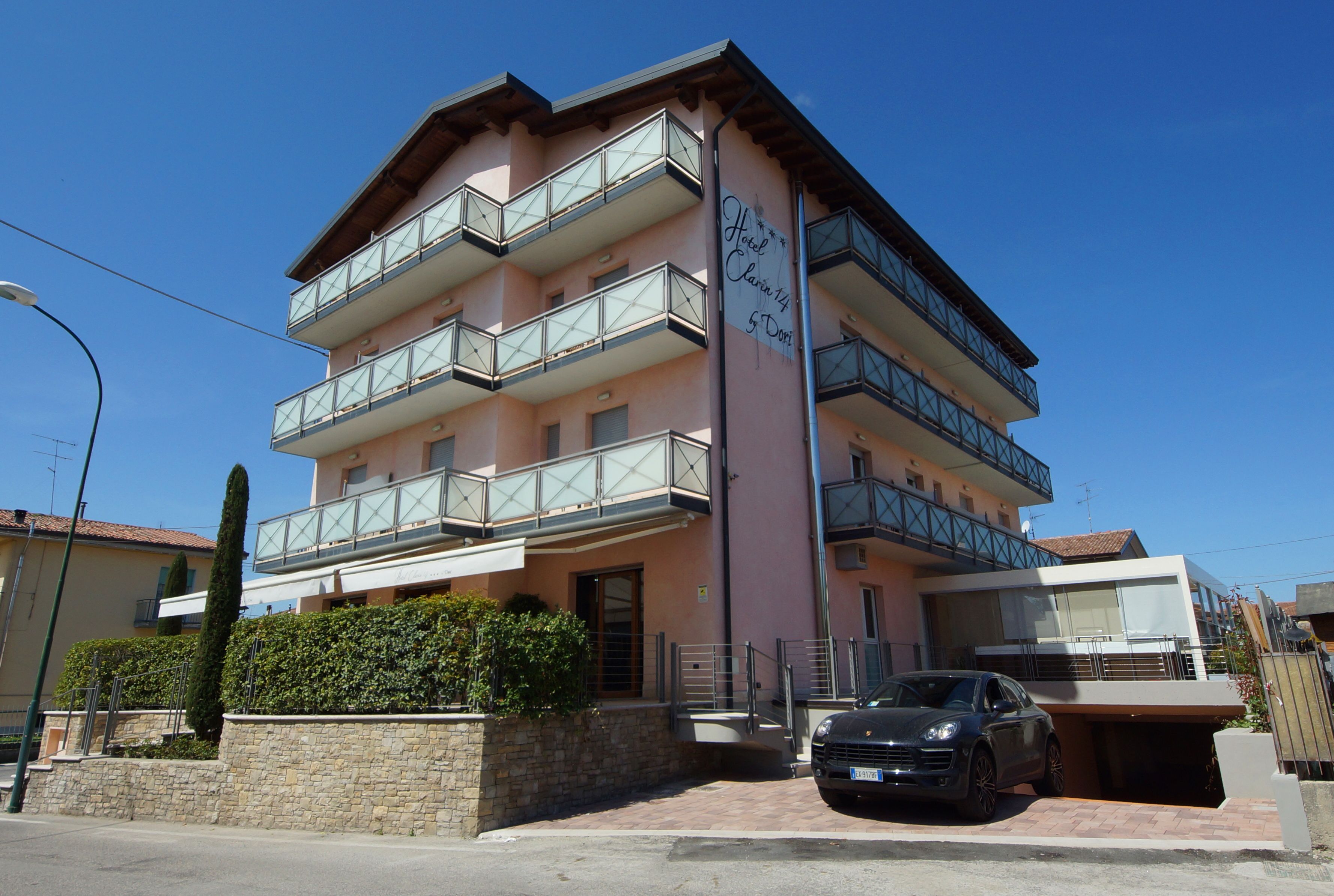 A multi-story hotel with balconies, a car parked in front, and a clear blue sky.