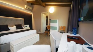 A hotel room with a bed, a sofa, a desk with a chair, a TV, and a bathroom visible in the background.