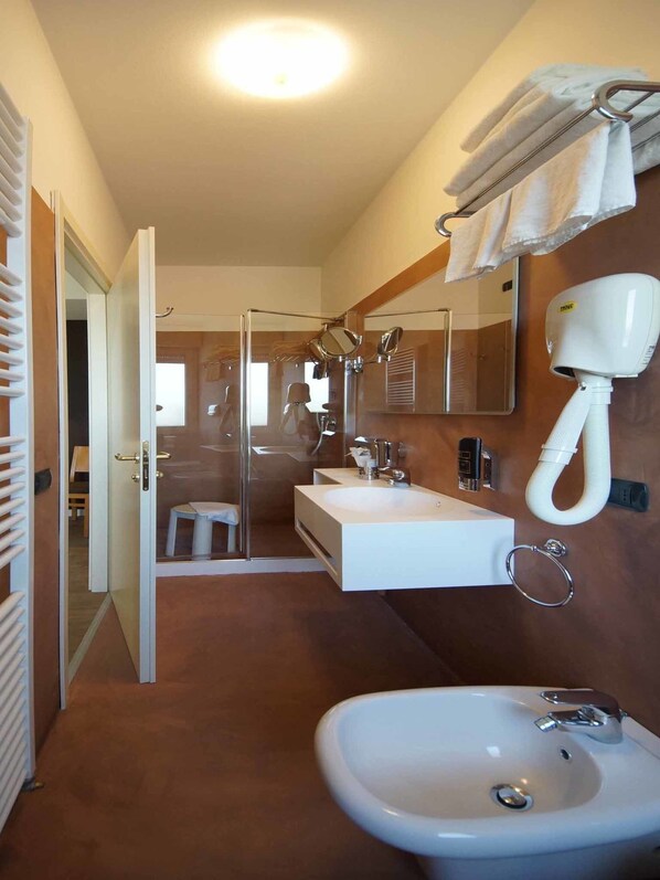 A modern bathroom with a glass shower, a white sink, and a hairdryer mounted on the wall.