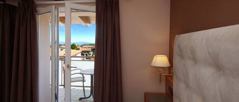 A hotel room with a bed, a nightstand with a lamp, a view of the outdoors, and a sliding door.