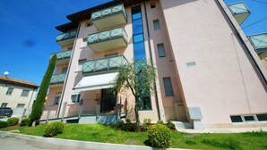 A multi-story building with balconies, a small garden area, and a clear blue sky.