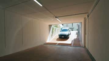 A parking garage with a car in the distance, concrete walls, and a sloped ceiling.