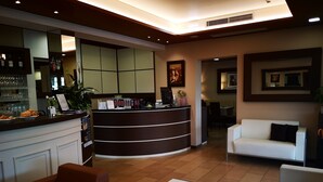 A reception area with a curved counter, seating area with white and brown sofas, and a bar with shelves of bottles and glasses.