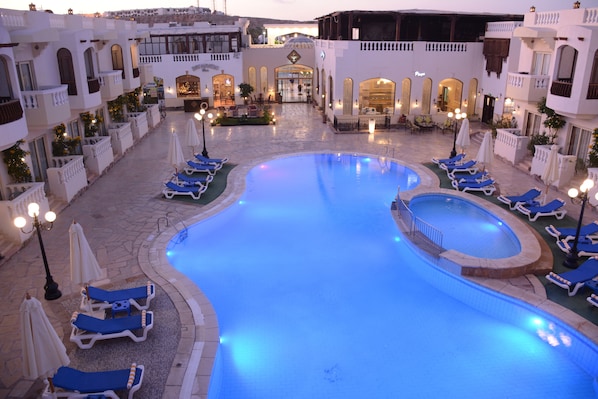 A pool area with lounge chairs and umbrellas, surrounded by buildings with arched windows and balconies. - Oriental Rivoli Hotel & SPA (Sharm El Sheikh)