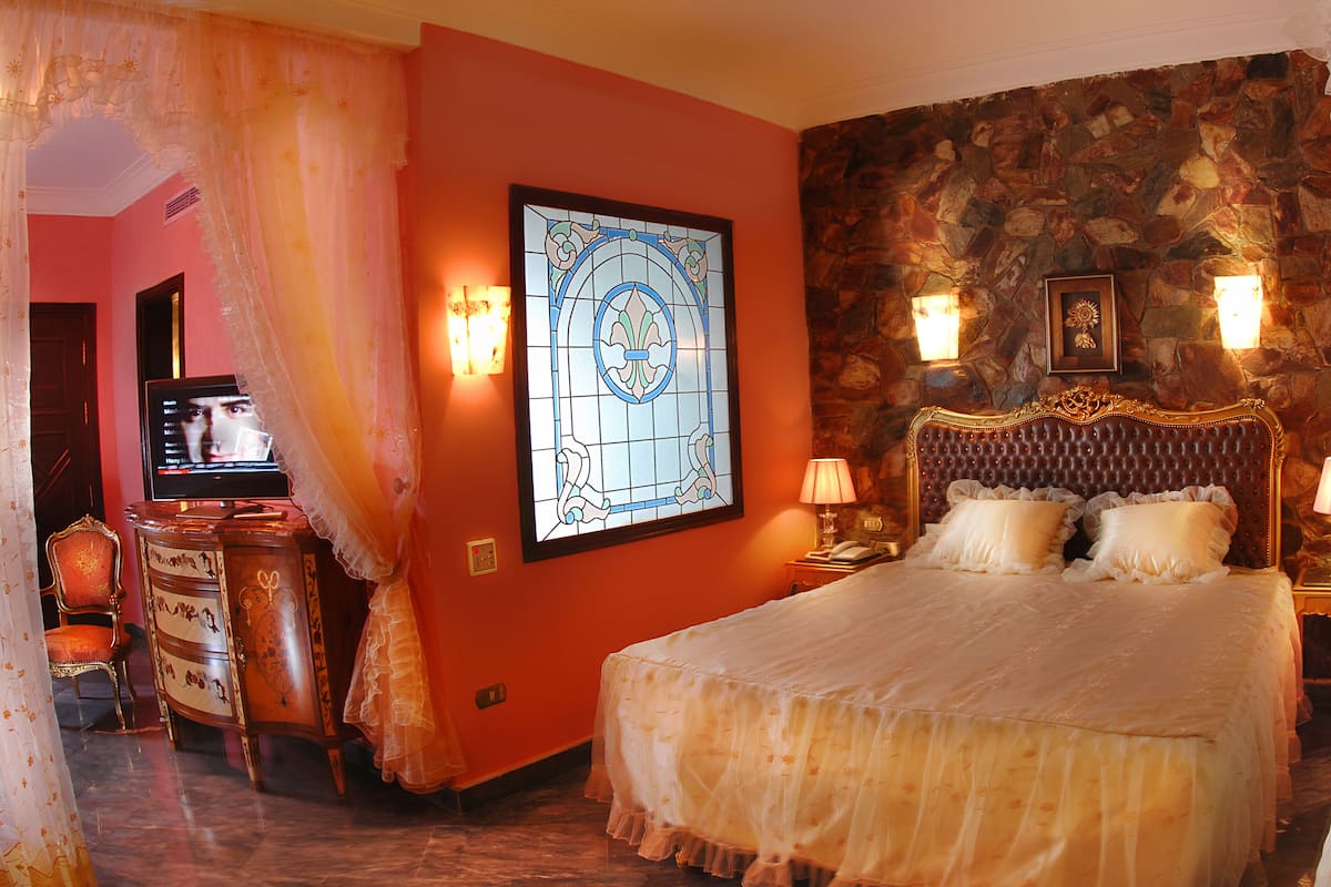 Ein Hotelzimmer mit einem großen Bett, einer Steinwand und einem Buntglasfenster.