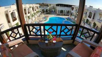 Un balcón con muebles de mimbre, una mesa con una bebida y vistas a una piscina y edificios.