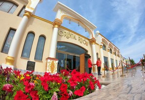The exterior of the Oriental Riviera hotel with a grand entrance, a marble pathway, and a red flower garden. - Oriental Rivoli Hotel & SPA (Sharm El Sheikh)