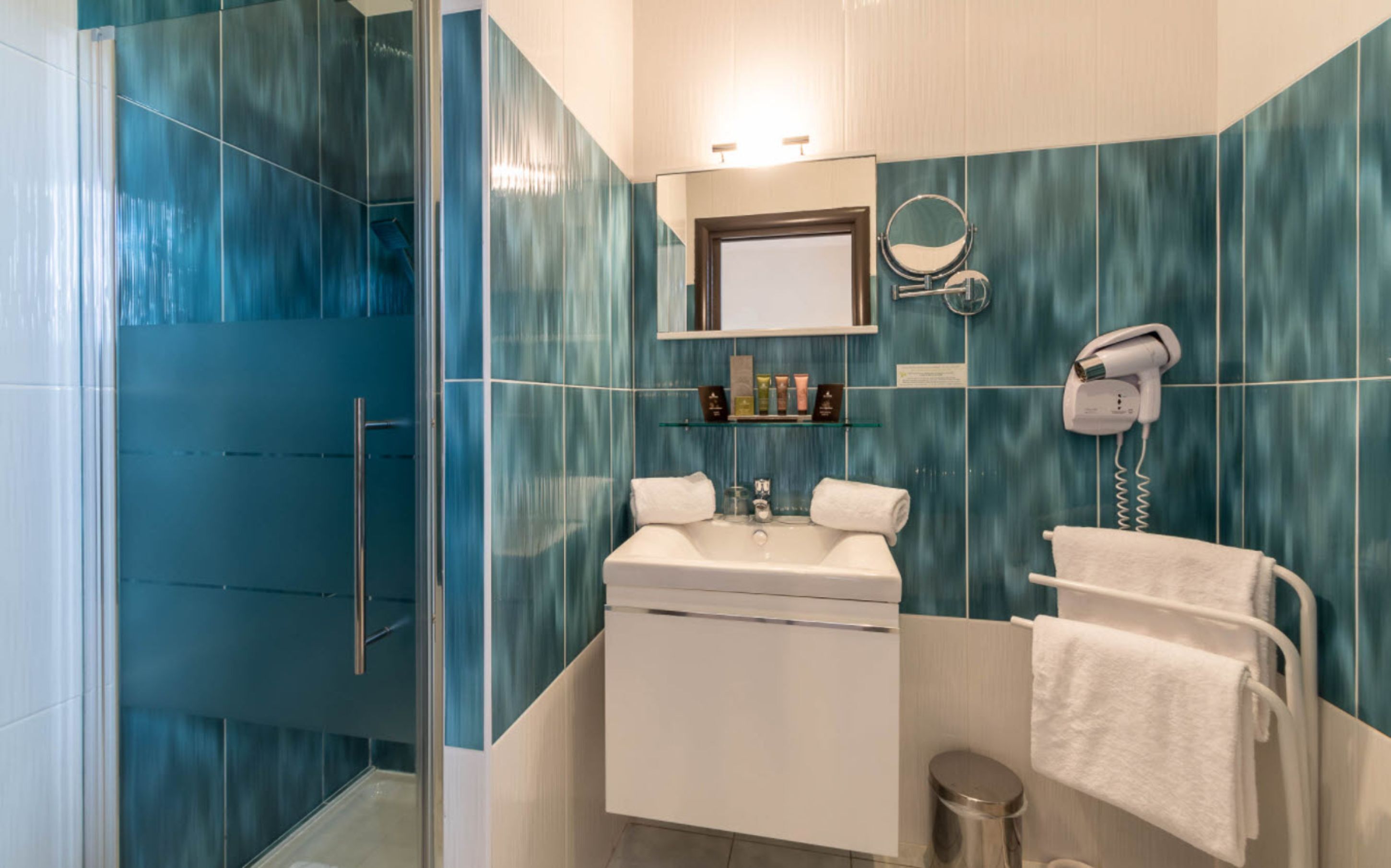 A modern bathroom with a glass shower enclosure, a sink with a mirror above, and a hairdryer on the wall.