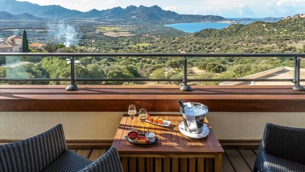 A balcony with a wooden table set for a meal, overlooking a scenic landscape with mountains and a lake. - A Casa Di Mà (Lumio)