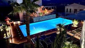 A swimming pool with a wooden deck, surrounded by palm trees and lounge chairs. - A Casa Di Mà (Lumio)