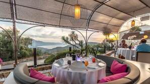 An outdoor dining area with a round table, cushioned seating, and a view of the landscape. - A Casa Di Mà (Lumio)