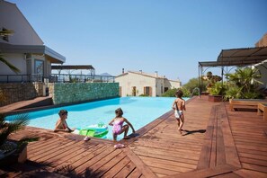 A wooden deck with a swimming pool, a stone wall, and a building with a tiled roof. - A Casa Di Mà (Lumio)