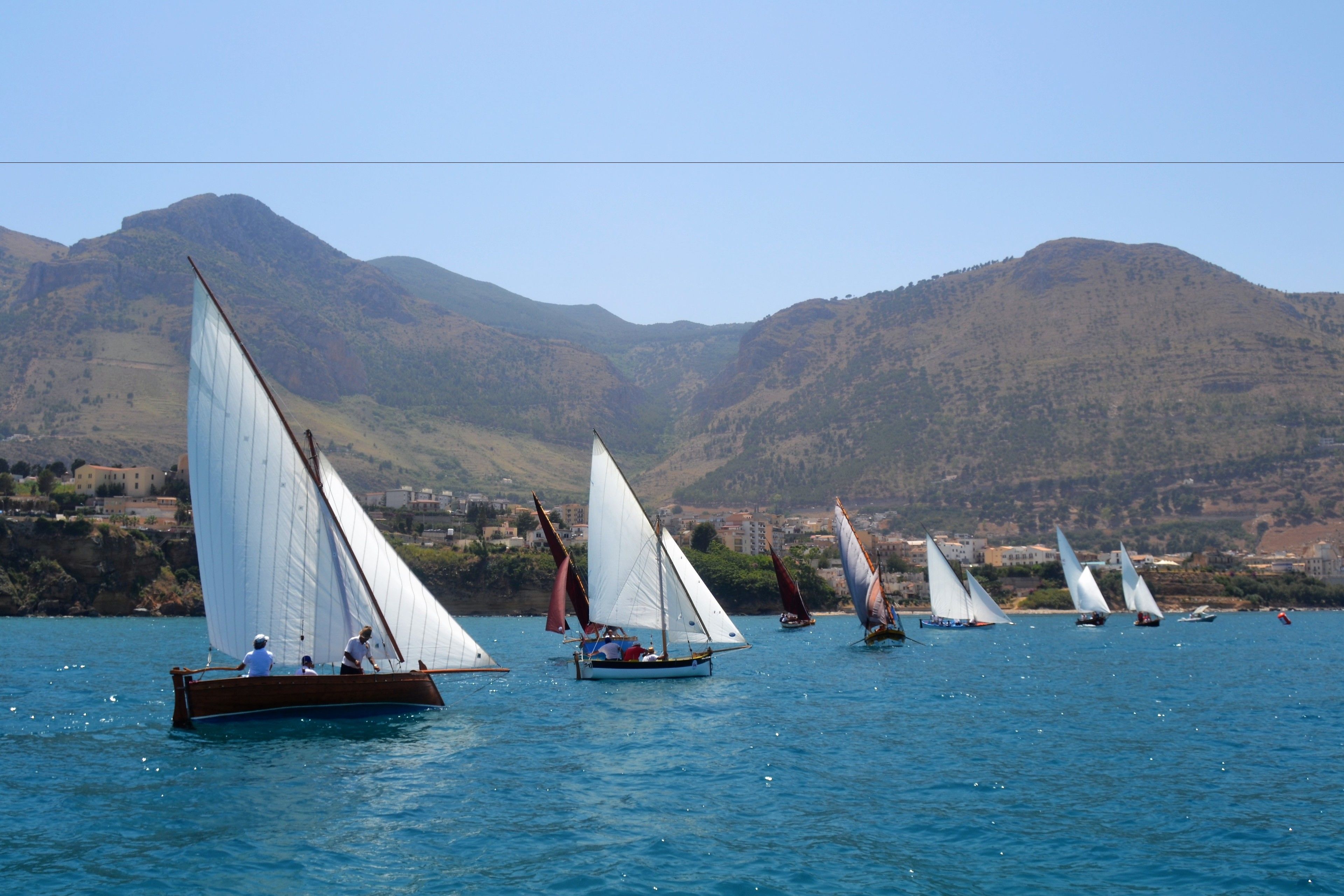 A group of sailboats on a calm lake with a mountainous backdrop.