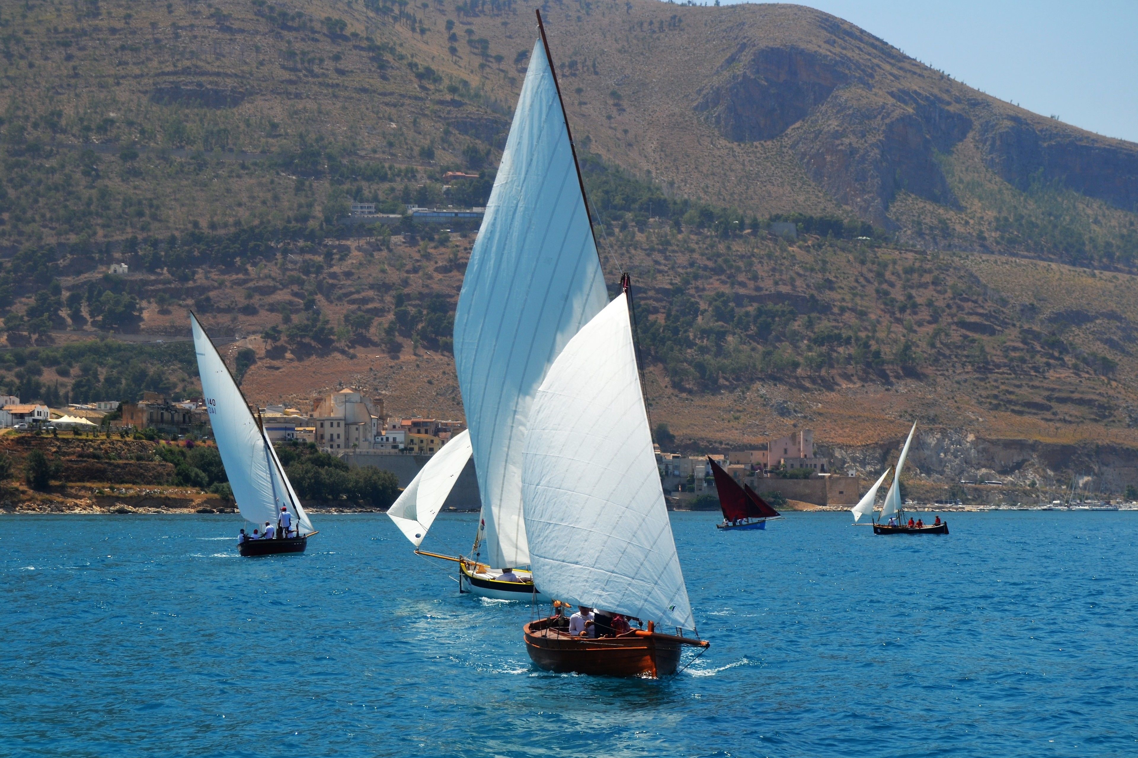 A coastal scene with sailboats on the water, a mountainous backdrop, and buildings along the shore.