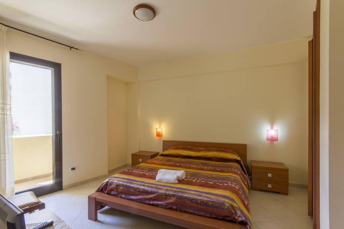 A bedroom with a bed, nightstands, a desk, and a window.