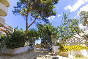 Une entrée fermée par un portail, avec un mur en pierre et un portail en bois, le tout entouré d’arbres et d’un parterre de fleurs.