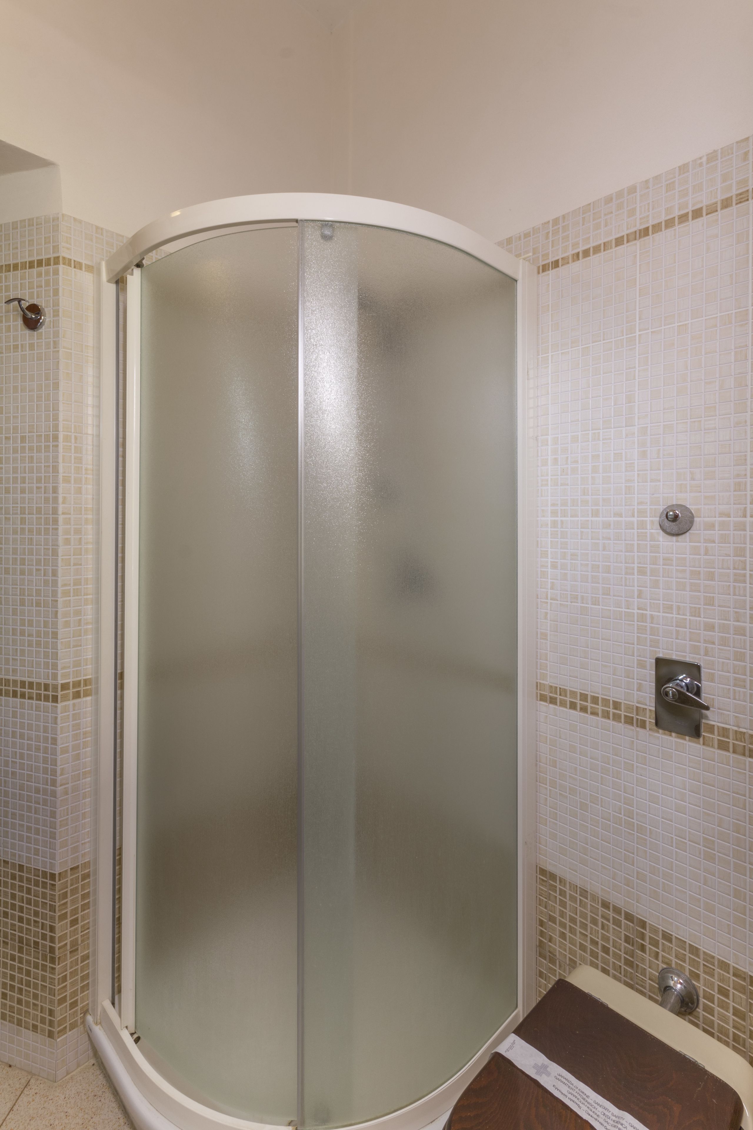 Une douche fermée par des parois de verre, avec un mur carrelé et un petit lavabo équipé d’un robinet.