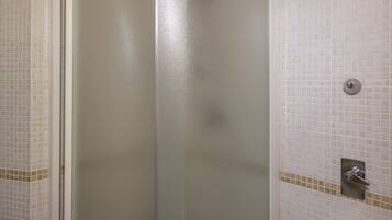 Une douche fermée par des parois de verre, avec un mur carrelé et un petit lavabo équipé d’un robinet.