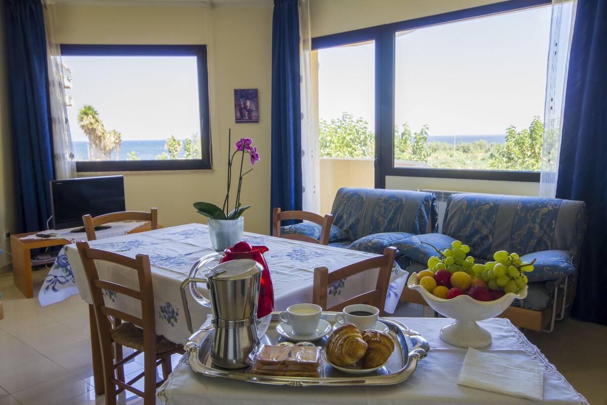 A dining area with a table set for breakfast, including croissants, fruit, and coffee.