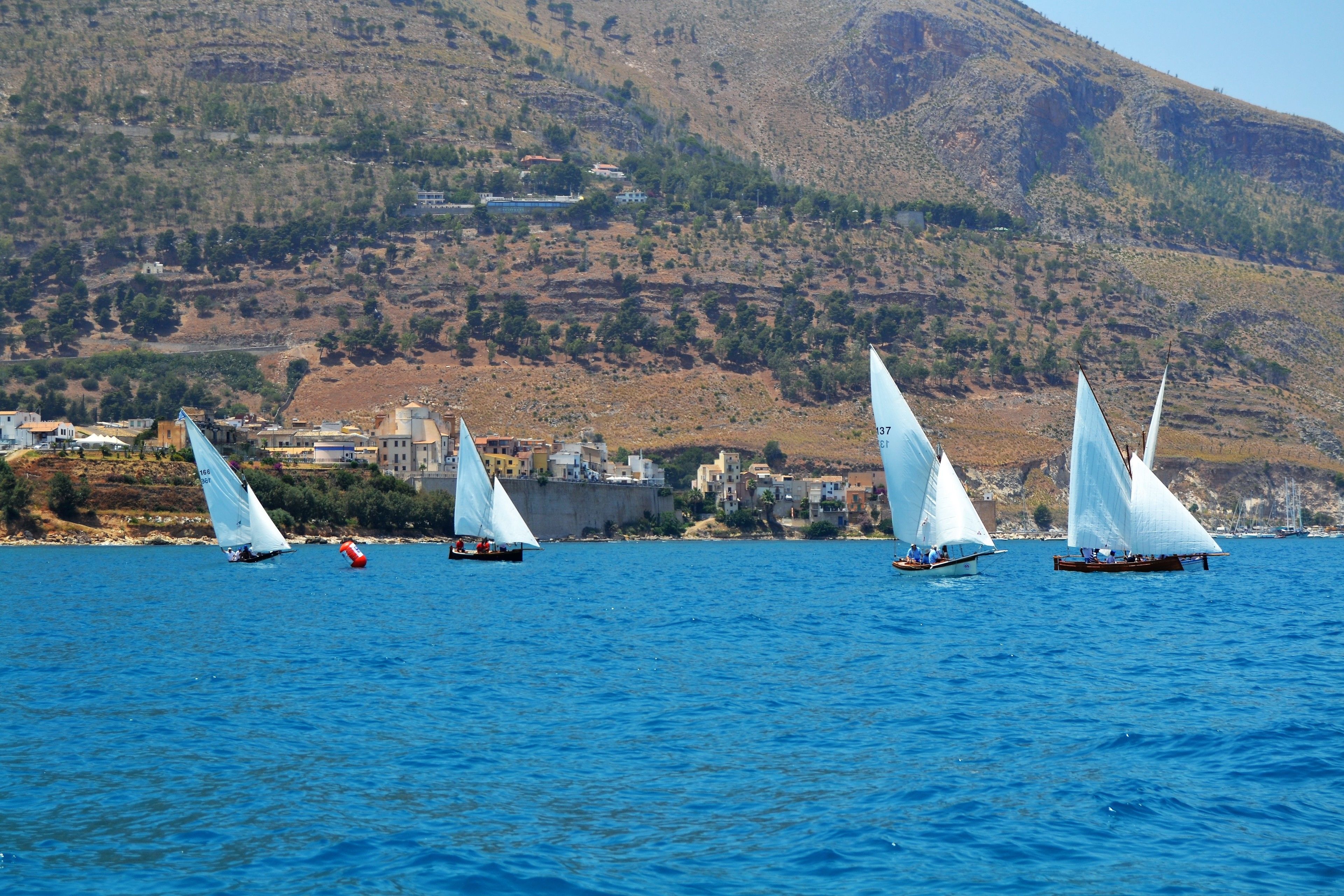 A coastal scene with sailboats on the water, a mountainous backdrop, and buildings along the shore.