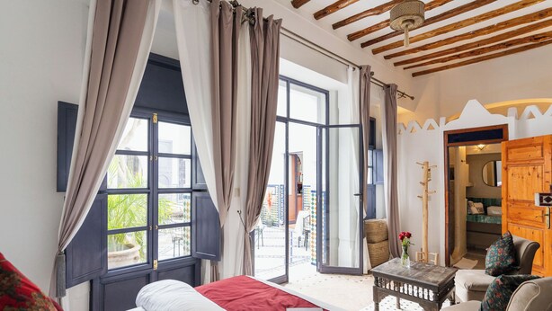 A bedroom with a bed, a wooden table, and a view of the outside. - Riad Twilight (Marrakech)