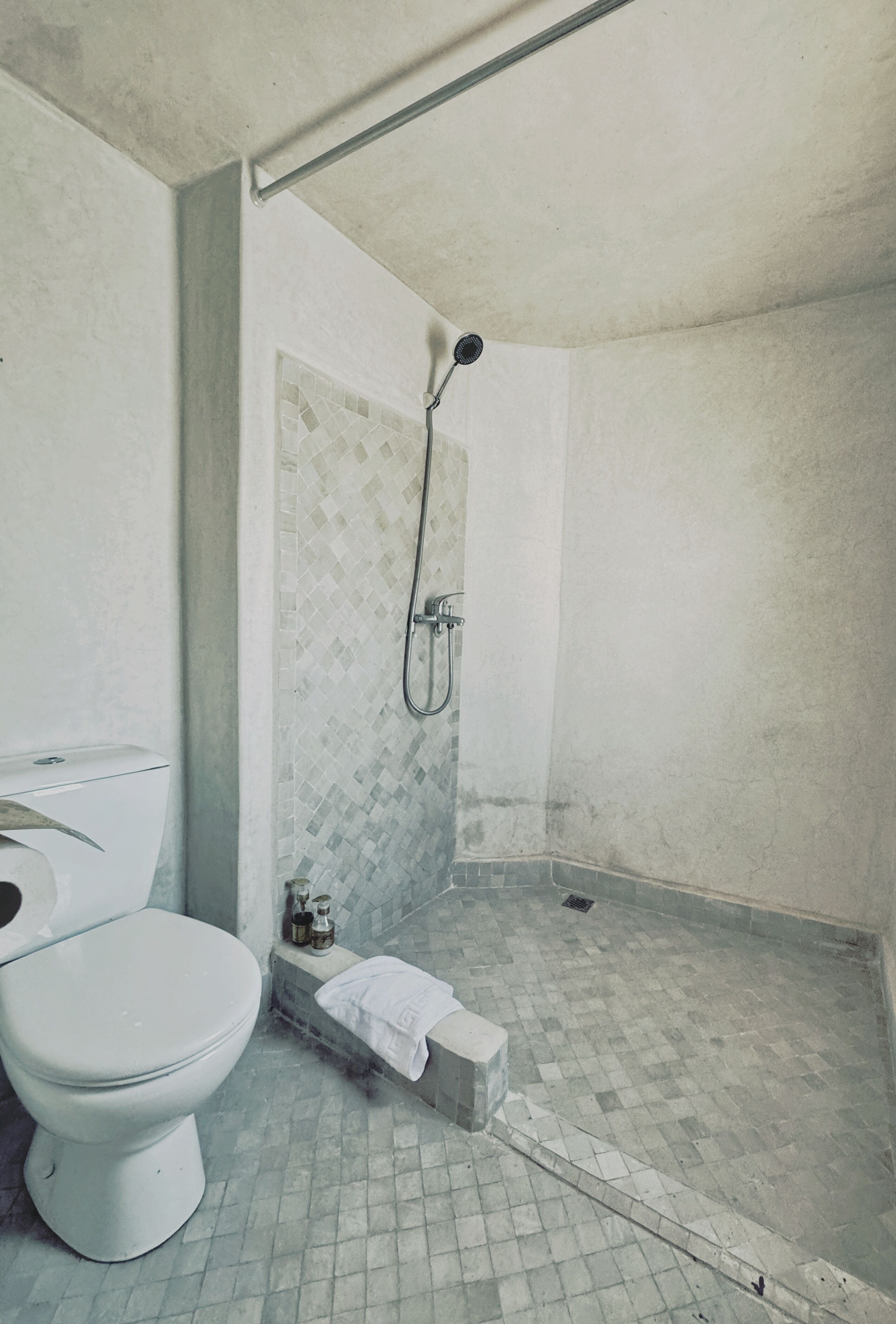 Un baño con inodoro, zona de ducha con pared azulejada y piso de baldosas.